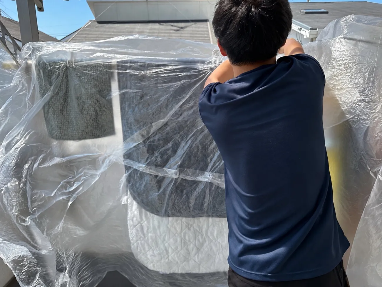 室外機洗浄や部品洗いのため、ベランダの周囲をシートで養生するスタッフ