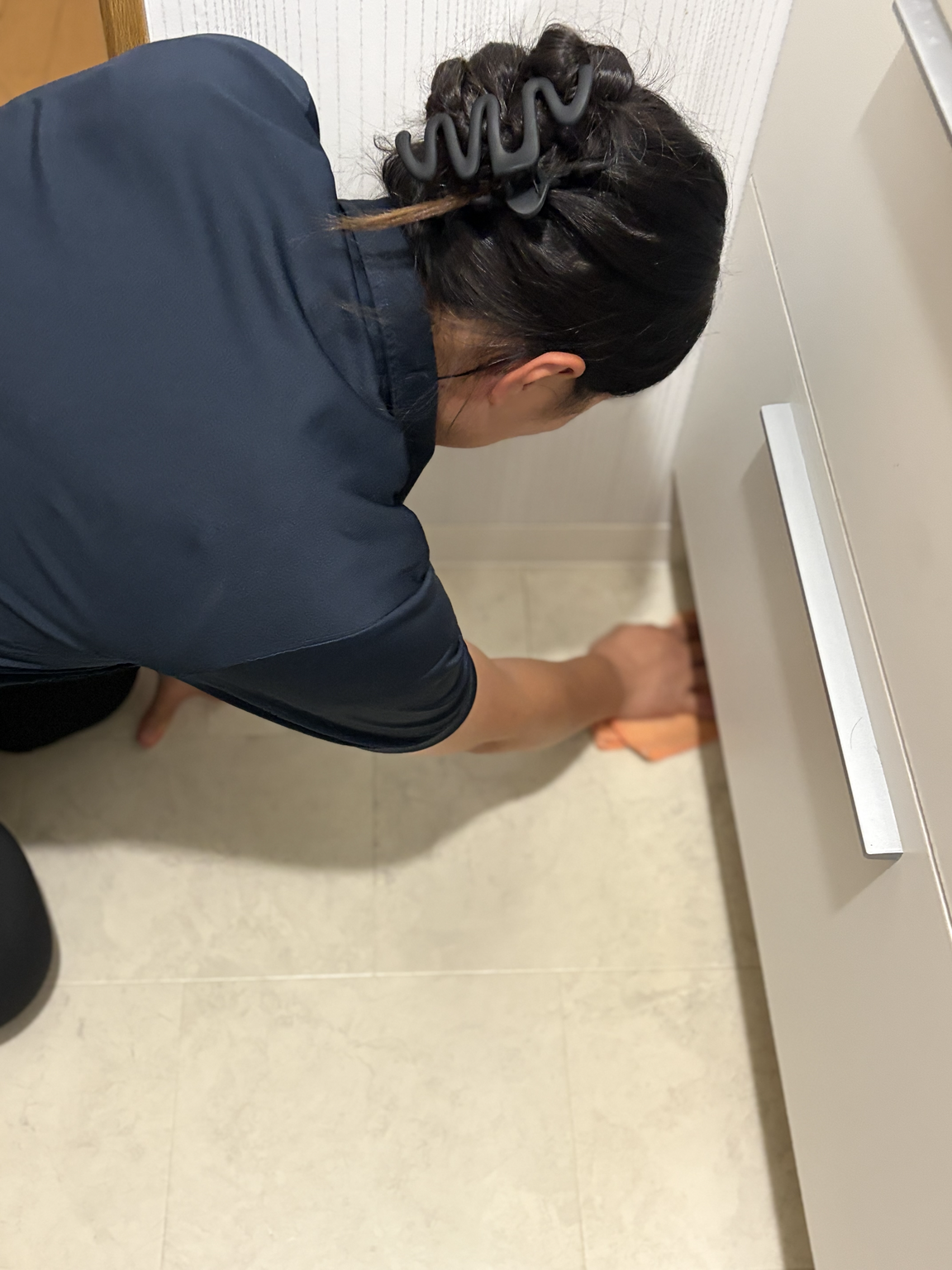 洗面台横の床際で周囲の状態を確認しながら清掃するスタッフ